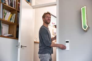 ABB zeigt Busch-Jaeger Schalter mit Doppelwippe, Einfachwippe und Temperaturregler-Display in weiß an einer hellgrauen Wand.