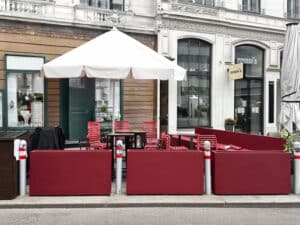 Eine Galerie bordeaux-roter Blumenkästen als Terrassenbegrenzung eines straßenseitigen Gastgartens von Blumentrog-Flexi.