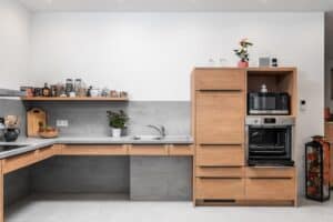 Eckküche „Andros“ mit Fronten in Holzoptik, schwarzen Griffleisten, Rückwand und Arbeitsplatte in grauer Betonoptik und integriertem Dunstabzug von DANKÜCHEN.