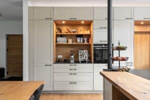 Landhausküche „Classico“ mit Kassettentüren in Hellgrau, schwarzen antiken Griffleisten, schwarzer Arbeitsplatte und Holz-Innenleben mit Spots von DANKÜCHEN.