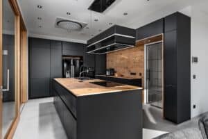 Moderne DAN-Inselküche Modell „Silbermond“ mit grifflosen Fronten in Anthrazit, Holzoptik-Rückwänden, rustikalen Arbeitsflächen, Dunstabzug und Deckenspots.