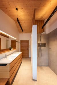 Obergeschoß-Badezimmer mit Holzdecke mit schwebendem Doppelwaschtisch und einer WC- und Duschnische von ERLER Haus.