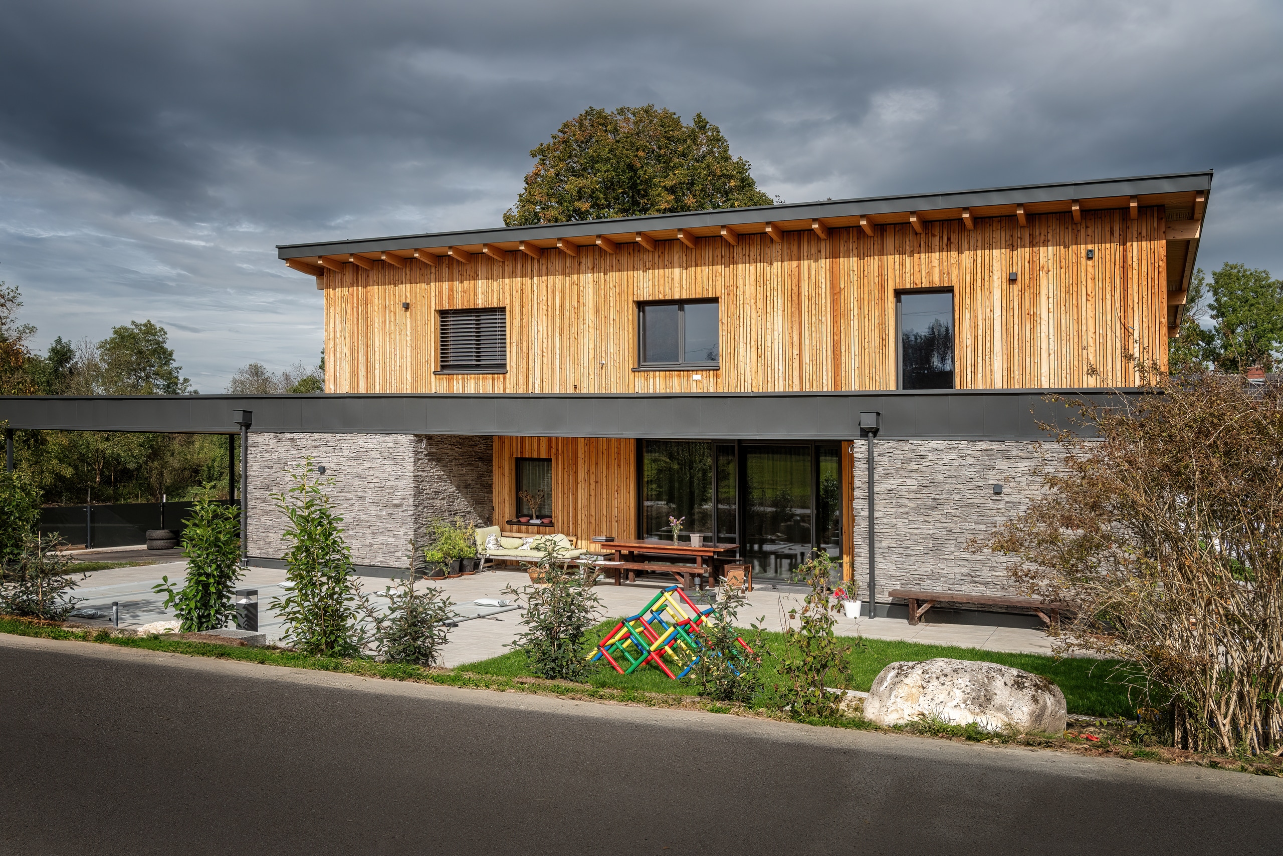 Einfamilienhaus mit Flachdach und Fassadenelement in Holzsprossenoptik, sowie Steinfassade im Erdgeschoss und einem überdachtem Terrassenbereich von ERLER Haus.
