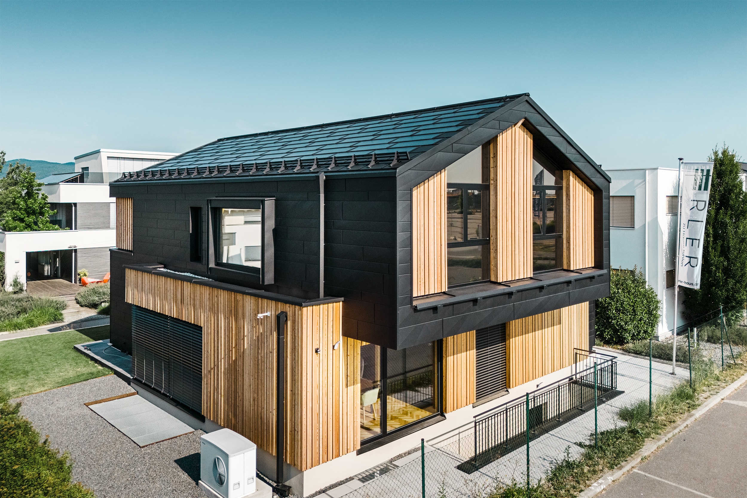 Einfamilienhaus "Autark" mit Satteldach, bodentiefen Fenstern und großflächigen Terrassenschiebetüren mit schwarzem Alurahmen, Fassadenelementen aus schwarzem Aluminium, Vollholzsichtwänden, einem Nurglasgeländer in der Loggia des Obergeschosses und einem großem überdachten Terrassenbereich von ERLER Haus.