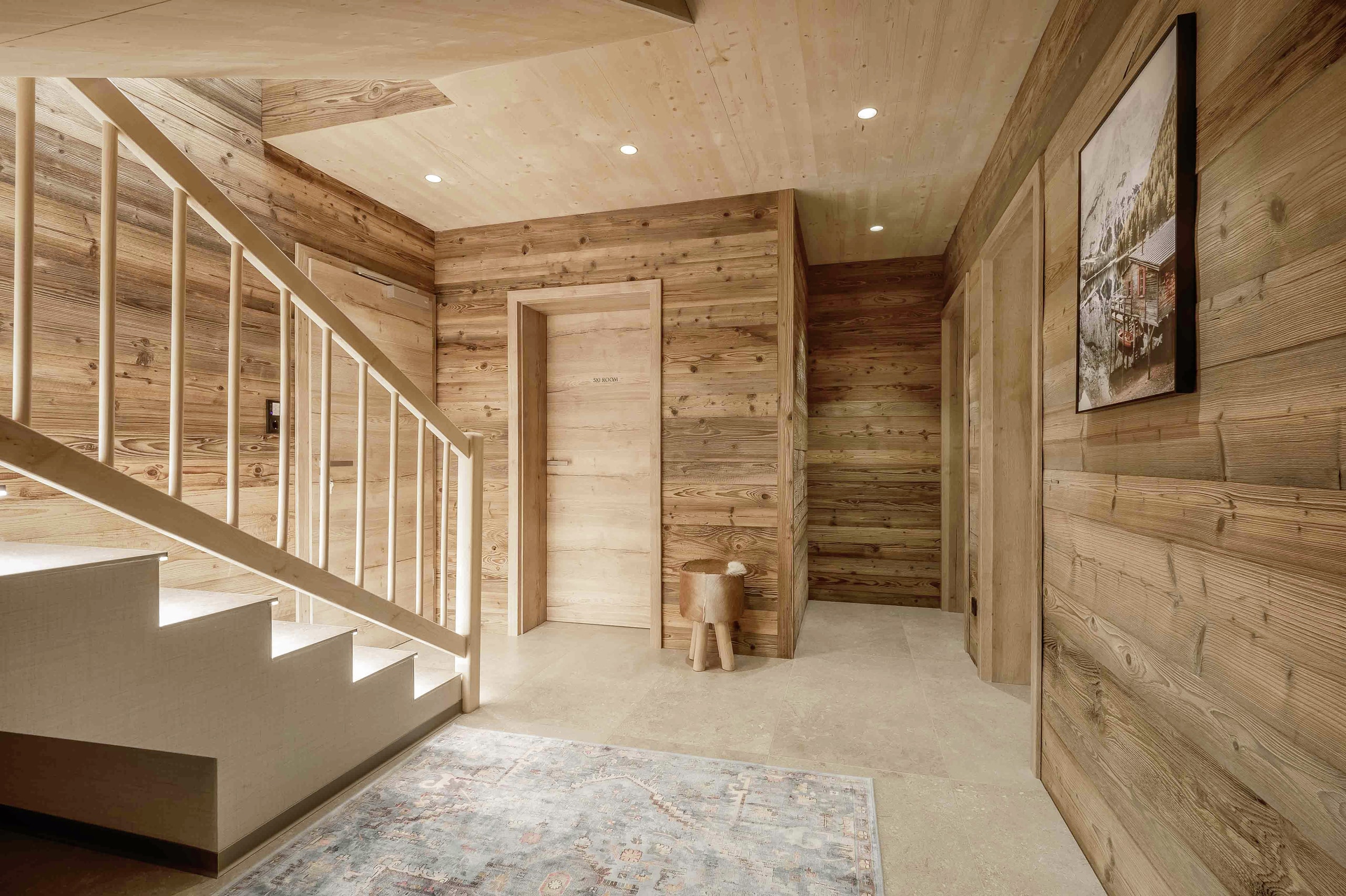 Eingangs- und Garderobenbereich eines Chalets mit holzverkleideten Decken und Wänden und einer Holztreppe von ERLER Haus.