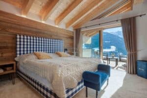 Schlafzimmer mit indirekt beleuchtetem Sichtdachstuhl, Teppichboden und Balkon mit Holz-Alu-Schiebetüren von ERLER Haus.