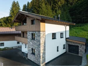 Ein mehrstöckiges Haus mit Satteldach und Fassadenelementen aus Holz und Stein, Wärmepumpe, überdachten Balkonen und angebauter Garage von ERLER Haus.