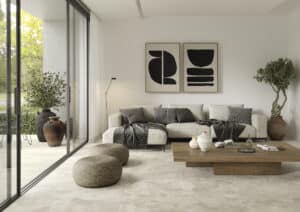 Ein Wohnzimmer mit beiger Sofalandschaft, grossem Holzcouchtisch, 2 Poufs, einer barrierefreien Terrassenschiebetür mit schwarzem Alurahmen und großformatigen Bodenfliesen in beiger Steinoptik im Innen- und im Außenbereich von Fliesendorf.