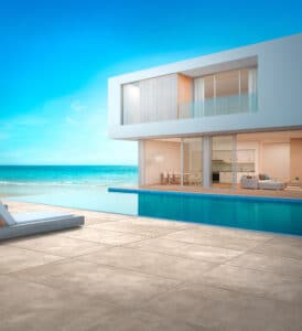 Fliesendorf zeigt die Aussenanlage einer Flachdachvilla mit Infinitypool mit rechteckigen Outdoorfliesen in beiger Steinoptik mit kontrastierender Patina.
