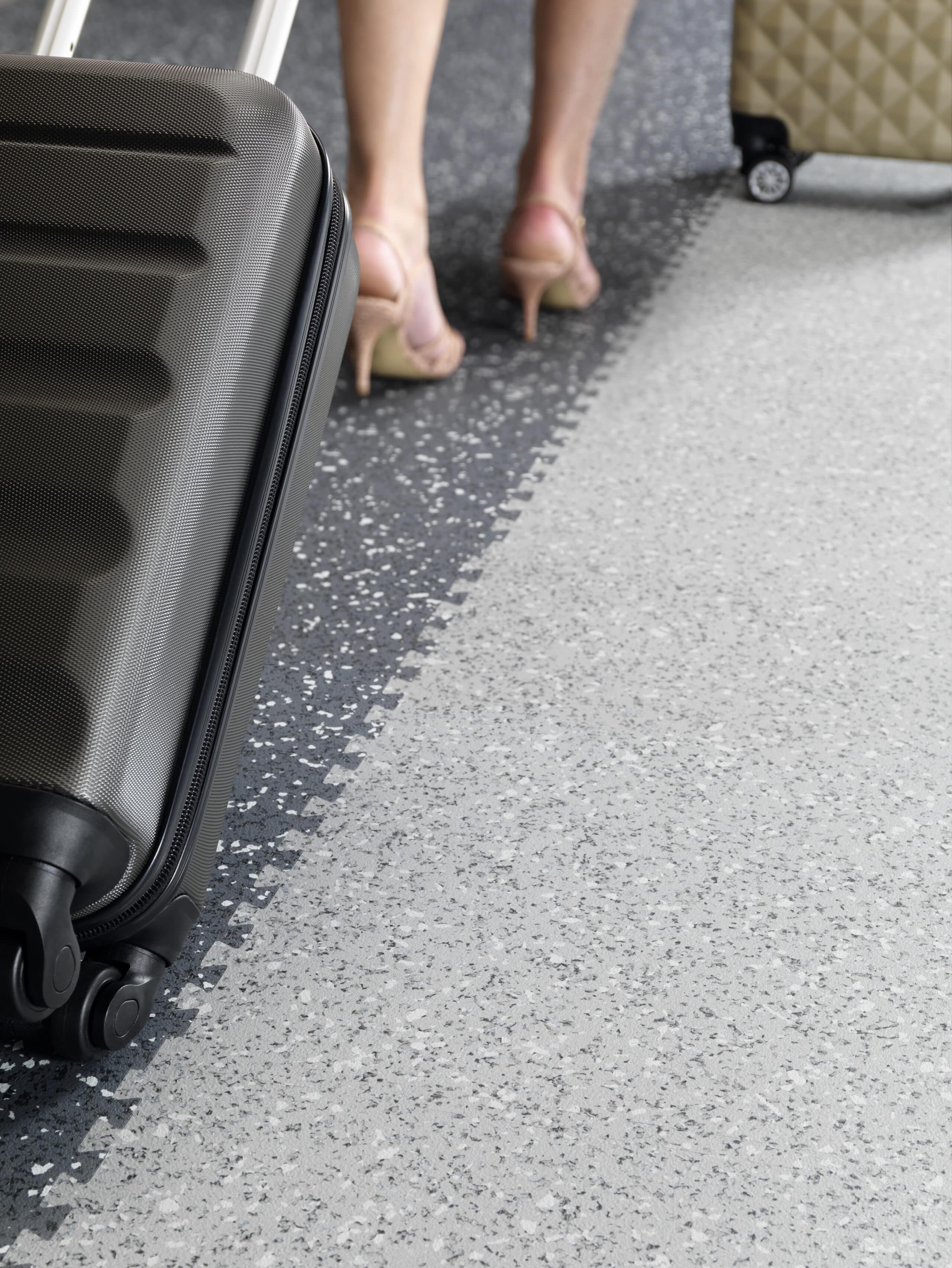 Gerflor präsentiert einen Bodenbelag in Grautönen in einem öffentlichen Gebäude, auf dem eine Dame in Stöckelschuhen geht.