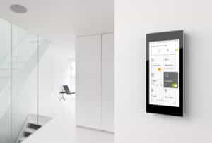 Ein wandmontiertes schwarzes G1 XS‑Bedien‑ und Anzeigegerät mit Glasfront zur Steuerung von Smart‑Home‑Funktionen im Wohnraum von Gira.