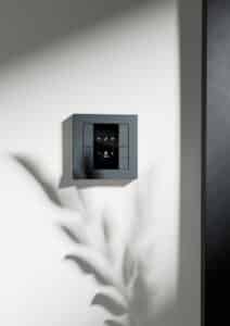 Ein Gira Schalter E2 TS4 55 2F in Anthrazit mit Anzeigedisplay an einer hellen Wand.