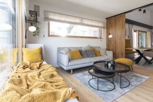 Hartl Haus zeigt gemütliches Wohnzimmer mit grauer Couch und großer gepolsterter Fensterbank vor großer Fensterfläche mit Blick in das Esszimmer.