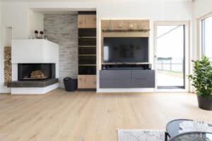 Wohnzimmer mit Naturparkett, Holzterrassentüren, wandmontiertem Medienboard und Kaminnische mit gemauertem Holzlager von HARTL HAUS.