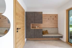 Ein Hauseingang mit einer Wand aus Garderoben- Schrank- und Sitzbankkombination gepolstert und aus Holz von HARTL HAUS.