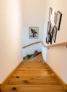 Eine Holztreppe mit geschwungenem Handlauf und einer Bildergalerie an den Wänden von HARTL HAUS.