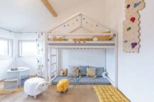 Ein kreativ gestaltetes Kinderzimmer mit Hochbett, integrierter Kletterwand und gemütlicher Spielecke unter einer Dachschräge von HARTL HAUS.