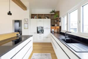 Eine moderne Einbauküche mit großzügiger Kücheninsel, integrierter Bar, Holzdetails und stilvollen schwarzen Armaturen von HARTL HAUS.
