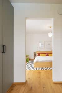 Ein gemütliches Schlafzimmer mit angrenzendem Ankleidezimmer mit maßgefertigtem Kleiderschrank in hellgrün für aufgeräumten Stauraum von HARTL HAUS.