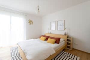 Ein helles Schlafzimmer mit Naturparkett, großzügiger Balkon- bzw. Terrassentür, natürlichem Lichteinfall und ruhiger, harmonischer Einrichtung von HARTL HAUS.
