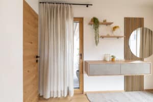 Ein Schlafzimmer mit Holzelementen und in Grautönen gehalten mit einer Kommode mit Spiegel und Wandpaneel und einem Vorhang über der Terrassentür von HARTL HAUS.