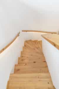 Ein heller Treppenaufgang mit eleganter gewendelter Holztreppe und geschwungenem Holzhandlauf von HARTL HAUS.