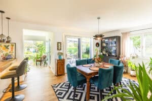 Eine helle Wohnküche mit Essbereich, Bar, Blick ins Wohnzimmer, großzügigen Glaselementen, Terrassentüren und gemütlicher Einrichtung von HARTL HAUS.