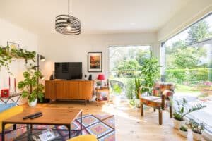 Ein farbenfrohes Wohnzimmer großzügigen Glaselementen, vielen Pflanzen und rustikalen Holzmöbeln von HARTL HAUS.