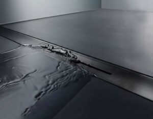 Hutter & Lechner zeigt eine eingebaute schwarze flächenbündige Duschrinne, in die das Wasser über den Schlitzablauf abrinnt.