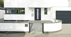 Eine moderne mattschwarze Haustüre mit satiniertem silbergerahmten Glasinnenteil von HÖRMANN und einem passenden mattschwarzen Garagentor in einem stilvollen, hell gestalteten Eingangsbereich.