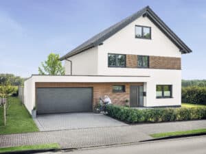 Ein modernes Einfamilienhaus mit Satteldach, ergänzt durch Holzelemente an der Fassade und einer anthrazitfarbenen Haustür und passendem Garagentor von HÖRMANN.