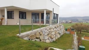 Einfamilienhaus mit großzügigem Garten in Hanglage und einem Glasgeländer über einer Steinmauer von Glaserei Hohl.