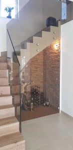 Eine Innenraumtreppe mit getöntem Nurglasgeländer und einem Untertreppenstauraum mit Glastüre genutzt zur Inszenierung von Wein und Accessoires von Glaserei Hohl.