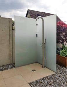 Garten mit Outdoordusche, großformatigen Bodenfliesen mit Wasserablauf und einer freistehenden, zweiseitigen, satinierten Vollglasduschwand von Glaserei Hohl.
