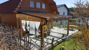 An ein Holzhaus angebauter Wintergarten aus Holzbalken und Glas mit Regenrinne, Pultdach und Glasschiebetüren von Glaserei Hohl.