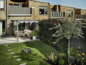 Husqvarna zeigt den Mähroboter Automower 305E NERA im Privatgarten einer Wohnung mit Terrasse.