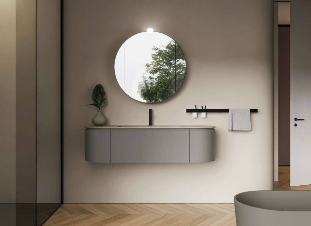 Ein Badezimmer mit grauem ovalen Unterschrank‑Waschtisch, Handtuchhalter und rundem Spiegel Design von Idea Group.