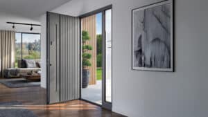 Eine geöffnete Inotherm-Haustür in Grau mit vertikalen Rillen und schmalem Seitenlichtfeld, die von innen fotografiert den Blick in einen modern eingerichteten Wohnbereich sowie durch die Tür auf eine Terrasse mit Holzlamellen-Fassade und Formgehölz freigibt.