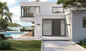 Eine moderne Inotherm-Haustür in Anthrazit mit horizontalen Glasstreifen aus satiniertem Glas und schmalem Seitenlichtfeld, integriert in eine minimalistische weiße Villa mit Pool, Holzdeck und tropischer Bepflanzung am Wasser.