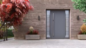 Eine moderne Inotherm-Haustür in Anthrazit mit vertikalem Edelstahl-Stoßgriff und beidseitigen Seitenlichtfeldern aus satiniertem Glas mit horizontalen Unterteilungen, eingebettet in eine horizontale Holzlamellen-Fassade, flankiert von Betonpflanzgefäßen mit Ziergräsern und einem rotlaubigen Zierbaum.
