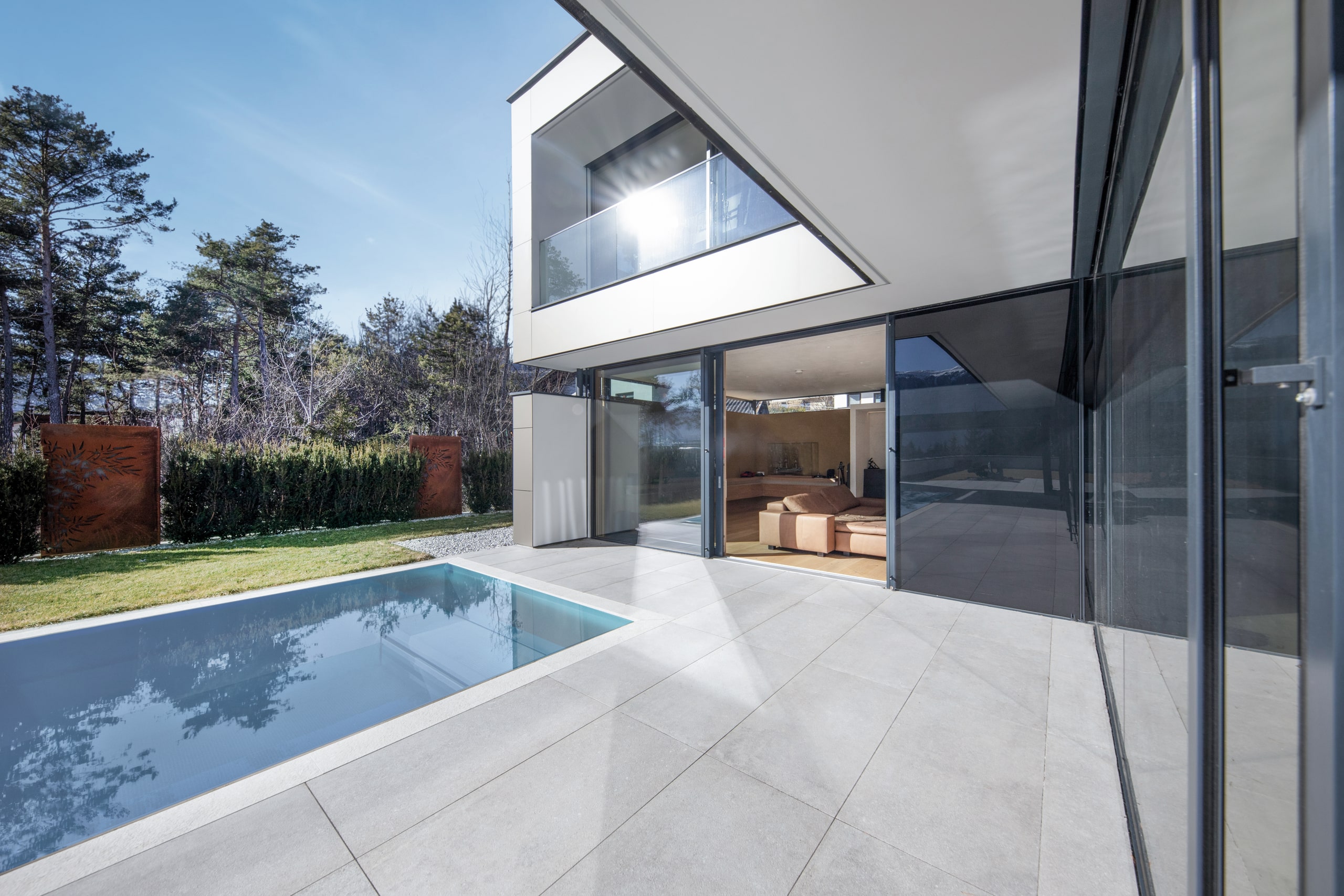 Internorm zeigt eine Villa mit Balkon und Glasgeländer und Ganzglassystem mit schwarzem Rahmen vor einer großen Terrasse mit Pool.