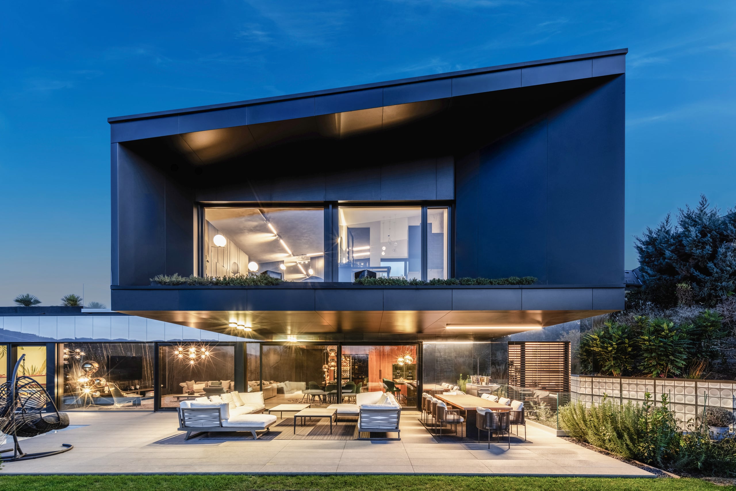 Eine moderne Villa mit überdachtem Terrassen- und Balkonbereich mit Schiebetüren und Fixverglasungen in schwarzem Alu-Rahmen von Internorm.