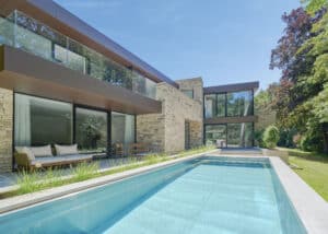 Eine moderne Villa mit Pool, Balkon mit Nurglasgeländer und einem Fassadenmix aus Stein und kupferfarbener Fassadenplatte von Internorm.