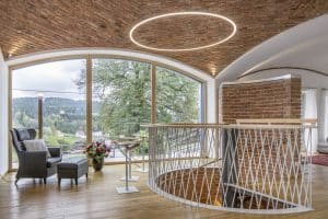 Gewendelte Treppe ins Obergeschoss eines offenen Wohnraumes mit verschiedenen Gewölbsarten und einer freistehenden gewölbten Ziegelwand von JAHN Gewölbebau.