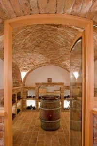 Gefüllter Weinkeller mit Gewölbe, einem Weinfass als Stehtisch und einer Glastüre mit Holzrahmen von JAHN Gewölbebau.
