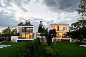 Ein modernes mehrstöckiges weisses Doppelhaus mit Flachdach, Fixverglasung, klaren Glaselementen mit schwarzem Rahmen, Kellerausbau und Garten mit Pool von Josko.