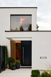 Ein modernes Einfamilienhaus mit Flachdach, großflächigen Glaselementen und einem seitlichen Lichtband am Hauseingang und Vordach von Josko.
