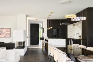Eine moderne Villa im Inneren mit schwarzer Hauseingangstüre mit Seitenlicht, einem offenen Wohnraum mit Wohnküche, elegantem Kamin sowie stilvollem Esstisch von Josko.