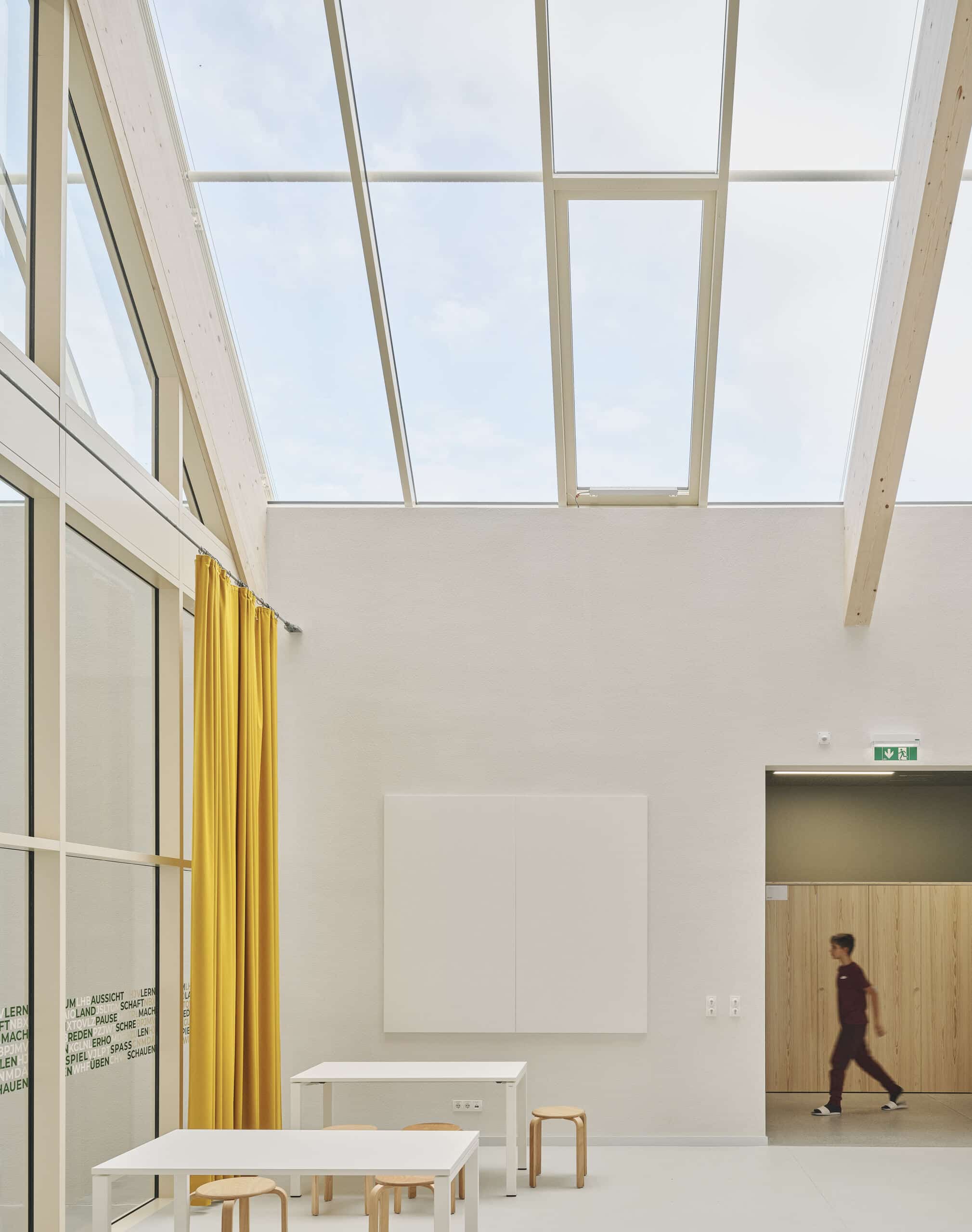 Lamilux zeigt den großen lichtdurchfluteten Gemeinschaftsbereich der Mittelschule in Graz-Puntigam mit großen schrägen Dachfenstern.
