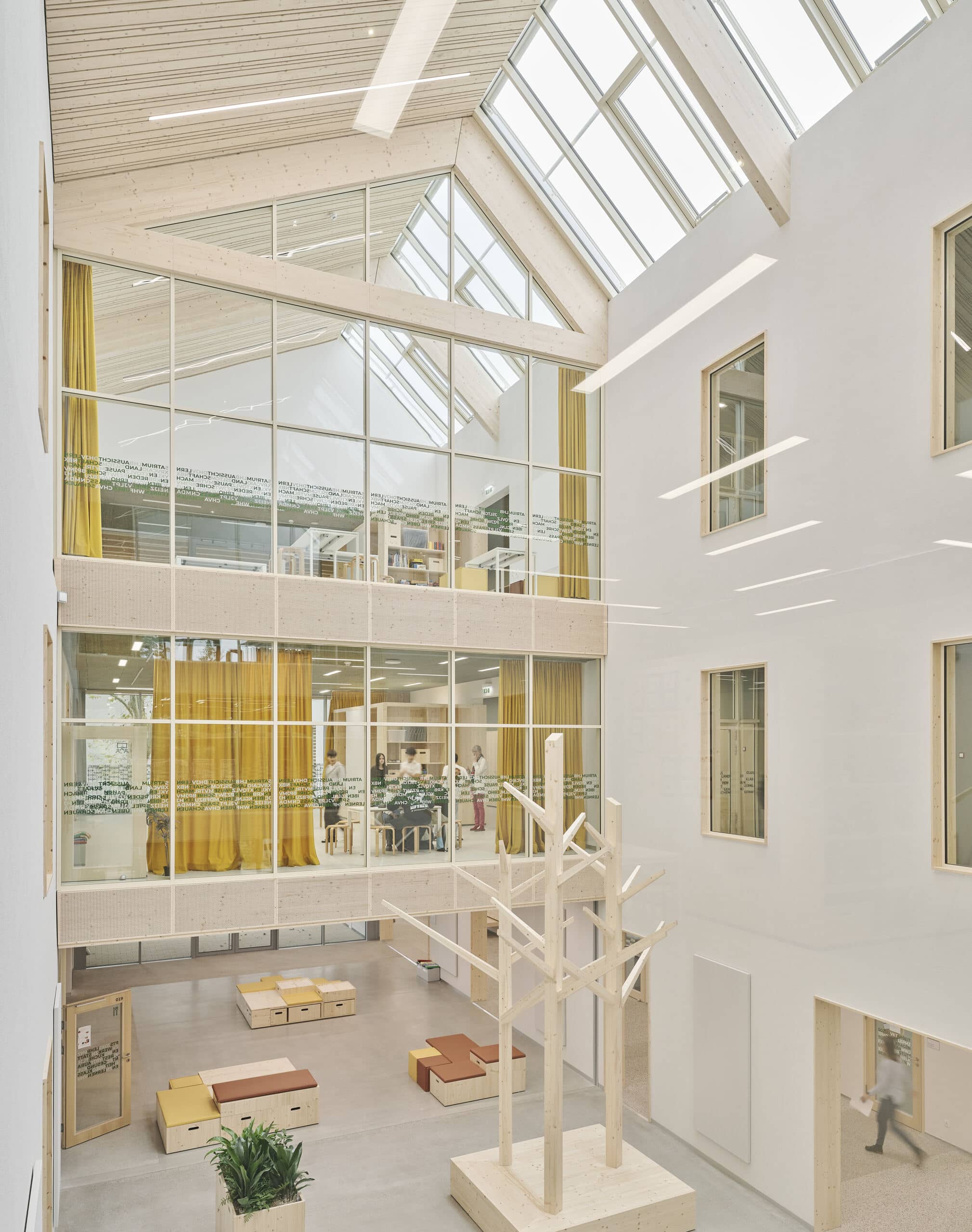 Lamilux zeigt den großen lichtdurchfluteten Gemeinschaftsbereich der Mittelschule in Graz-Puntigam mit großen schrägen Dachfenstern.